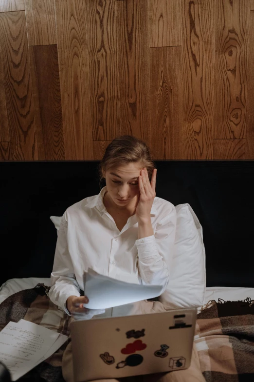 a woman sitting on a bed with a laptop, inspired by Elsa Bleda, trending on unsplash, renaissance, wearing a white button up shirt, with a sad expression, wearing a paper crown, hotel room