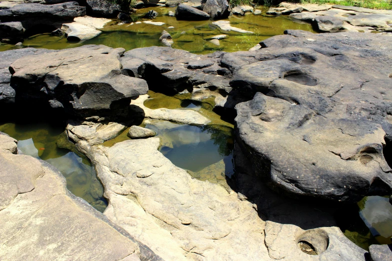 a group of rocks sitting on top of a river, by Elizabeth Durack, unsplash, bathing inside the tar pit, flagstones, rock plateau, very crisp details