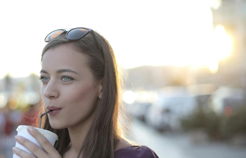 a woman drinking out of a paper cup, by Mathias Kollros, unsplash, holding a small vape, handsome girl, evening sun, promo image