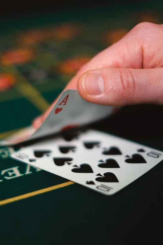 a person holding a playing card in front of a casino table, square, thumbnail, photograph