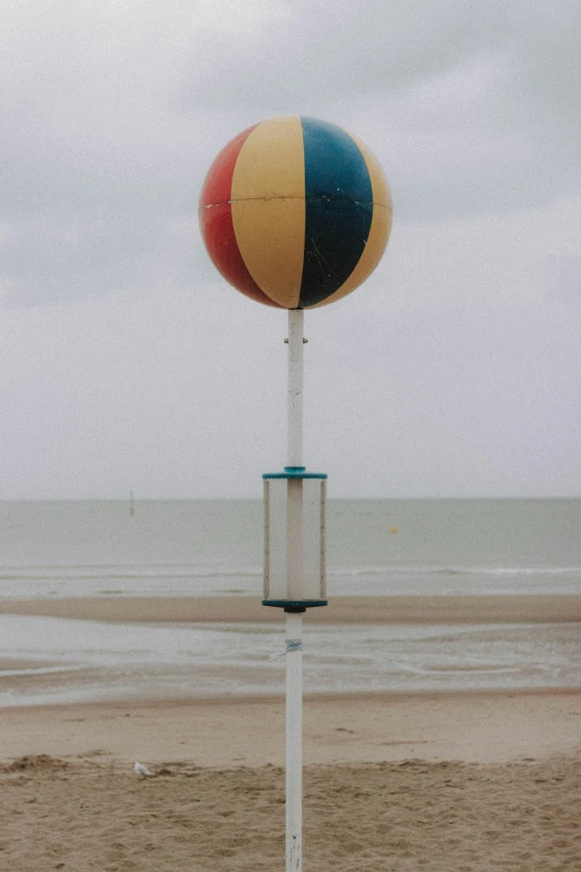 a beach ball sitting on top of a pole on a beach, inspired by Storm Thorgerson, unsplash, overcast!!!, northern france, b - roll, lantern