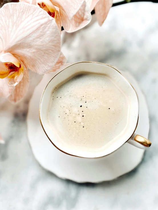 a cup of coffee and some flowers on a table, a portrait, by Lucia Peka, trending on unsplash, baroque, orchid made of mother of pearl, vanilla smoothie explosion, detailed product image, soft pale golden skin