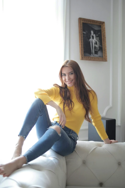 a woman sitting on top of a white couch, inspired by Olga Rozanova, instagram, felicia day, yellow, jeans, portrait image