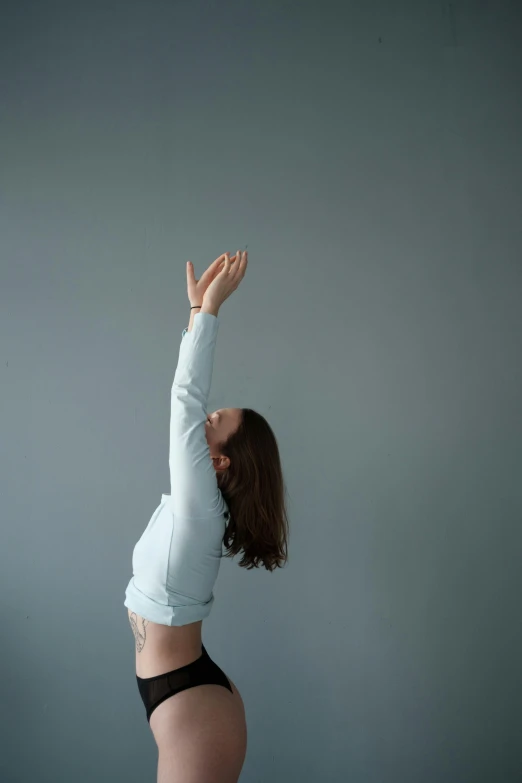 a woman in a white shirt is doing a yoga pose, an album cover, unsplash, grey backdrop, raised hand, blue, 15081959 21121991 01012000 4k