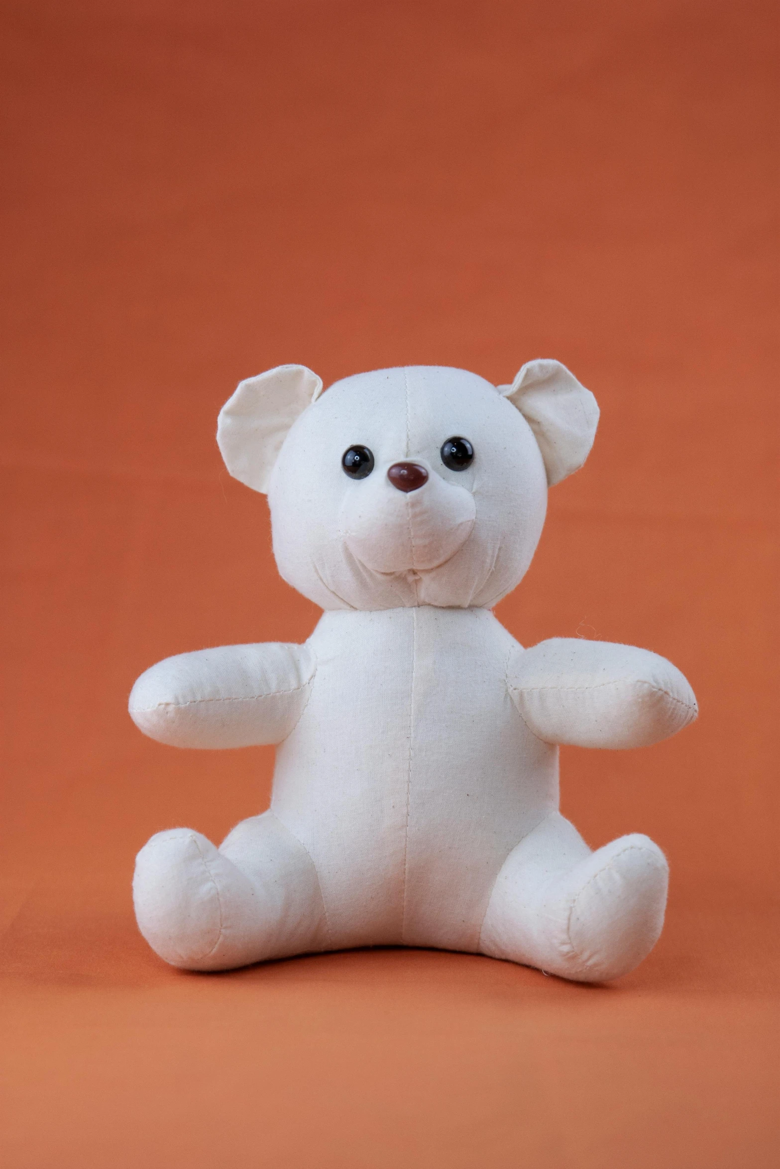 a white teddy bear sitting on an orange background, bangalore, ready to model, plushie, ready