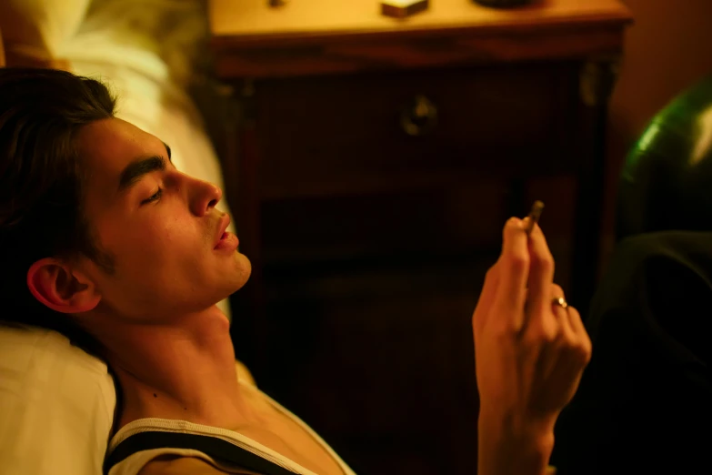 a man laying on a bed with a cigarette in his hand, a portrait, inspired by Nan Goldin, trending on pexels, fantastic realism, robert sheehan, smoking a bowl of hash together, lily collins, animation still