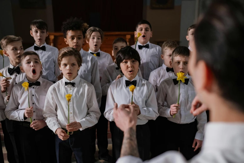 a man standing in front of a group of children, an album cover, inspired by Louis Le Nain, pexels contest winner, antipodeans, scene set in a church, cute boys, blossoming rhythm, ( ( theatrical ) )