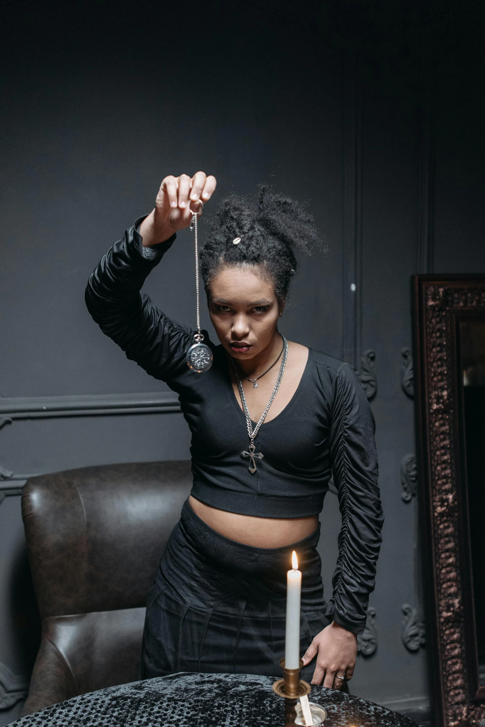 a woman lighting a candle on a table, an album cover, trending on pexels, black arts movement, wearing modern gothic clothes, leather jewelry, foreboding room, hanging out with orbs