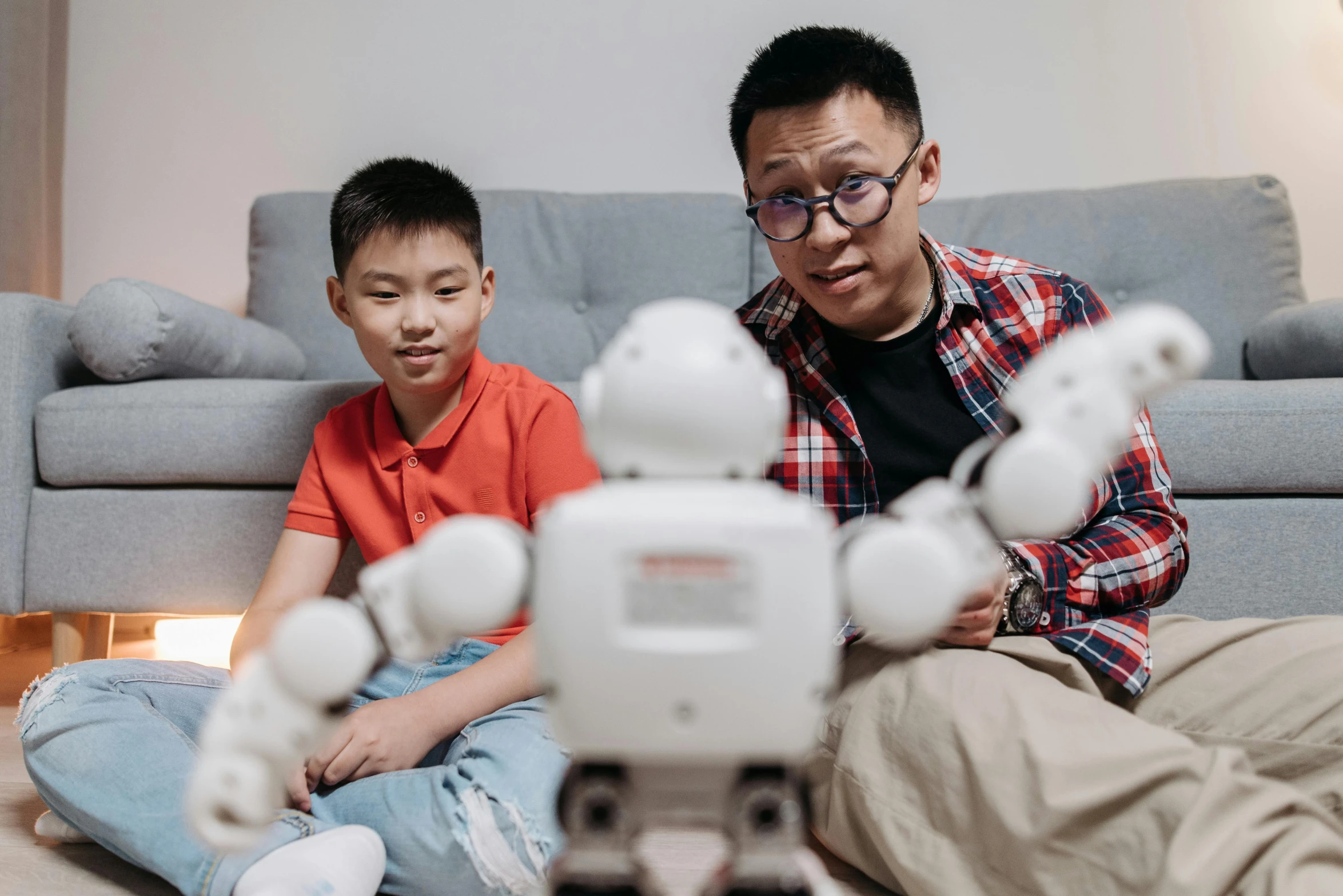 a man and a boy sitting on the floor next to a robot, pexels contest winner, darren quach, teaching, avatar image, looking across the shoulder