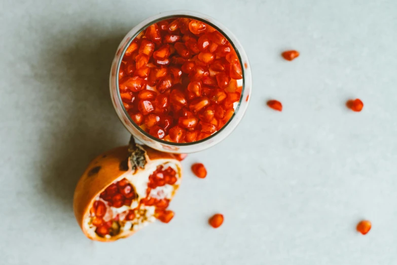 a close up of a pomegranate on a table, a still life, by Emma Andijewska, pexels, baked beans, background image, inside a glass jar, flatlay