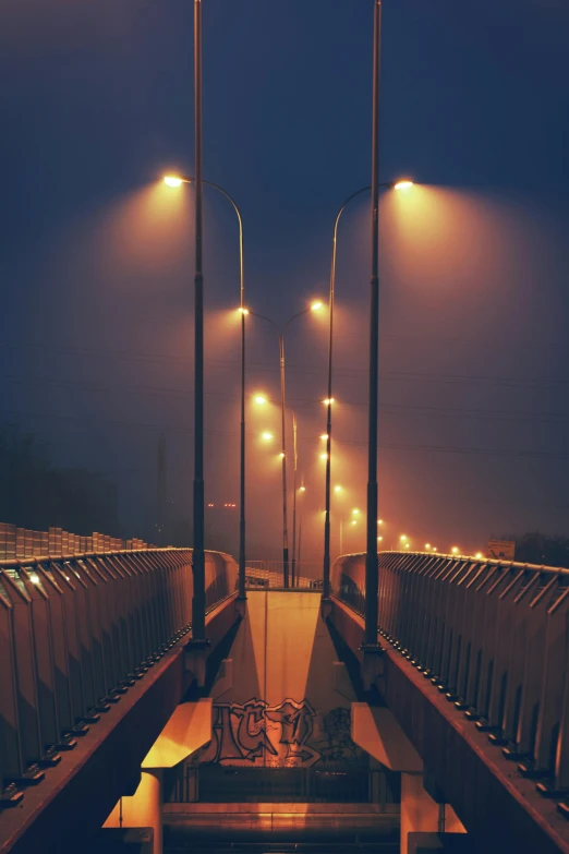 a bridge over a body of water at night, by Adam Marczyński, streetlamps, foggy twilight lighting, atmospheric lighting - n 9, wide