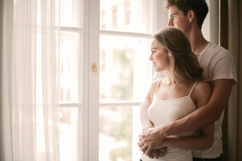 a man and a woman standing in front of a window, pexels, intimate holding close, white, attractive girl, where a large