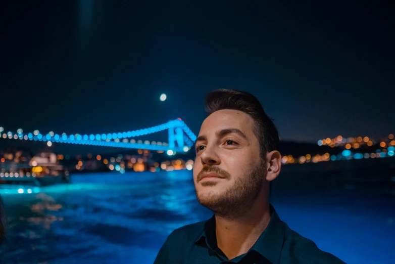 a man standing in front of a bridge at night, a picture, by Cafer Bater, hurufiyya, avatar image, close up portrait photo, professional profile photo, extremely realistic photo