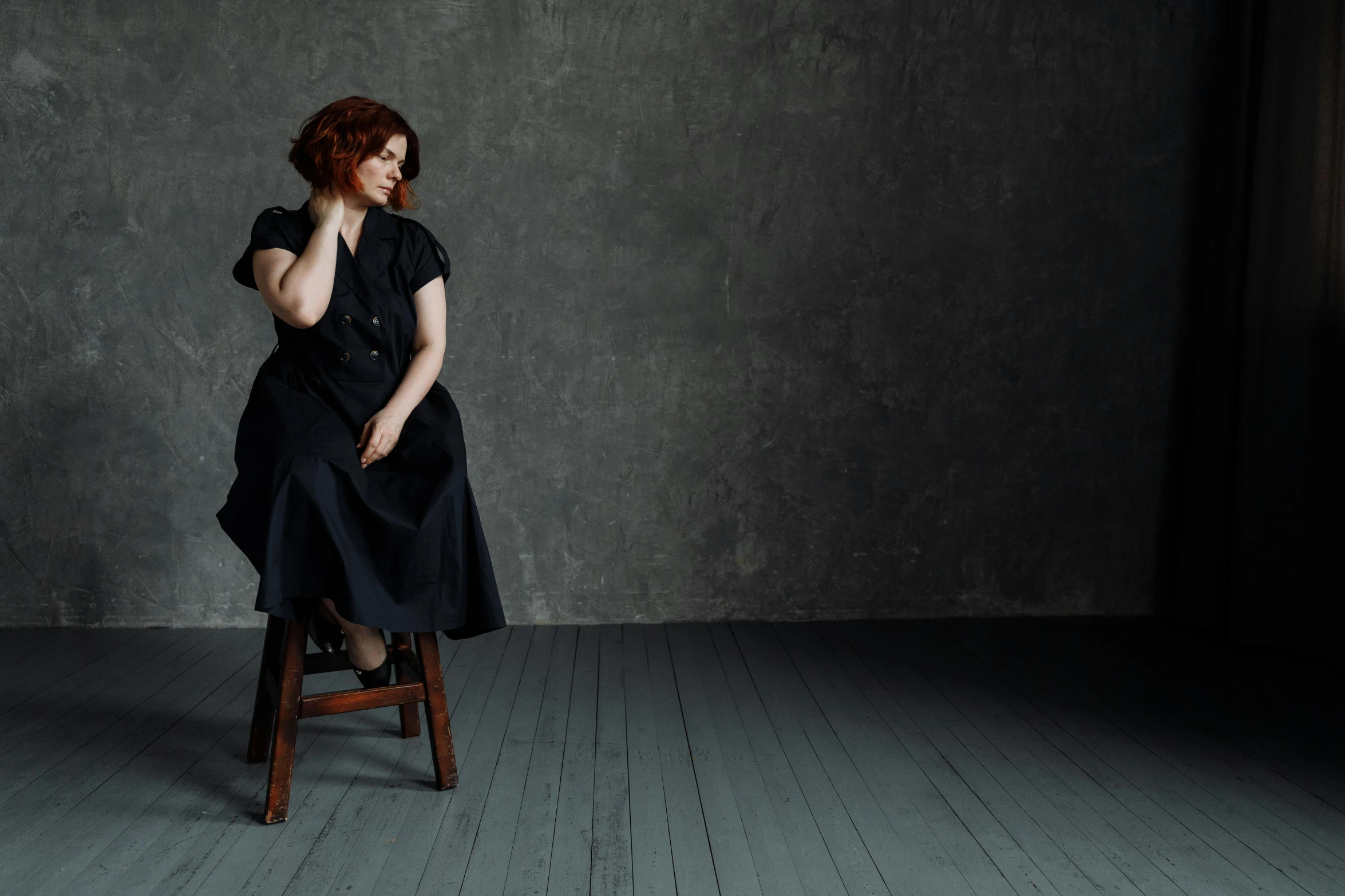 a woman sitting on top of a wooden chair, by Lucia Peka, unsplash, renaissance, christina hendricks, on a gray background, wearing a black dress, plus-sized