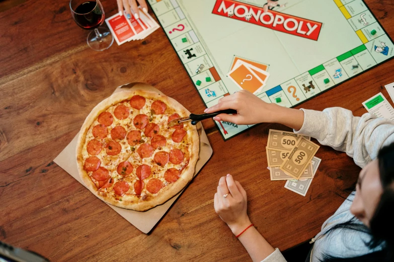 a couple of people sitting at a table with a pizza, game board, on a table, uncrop, multicoloured