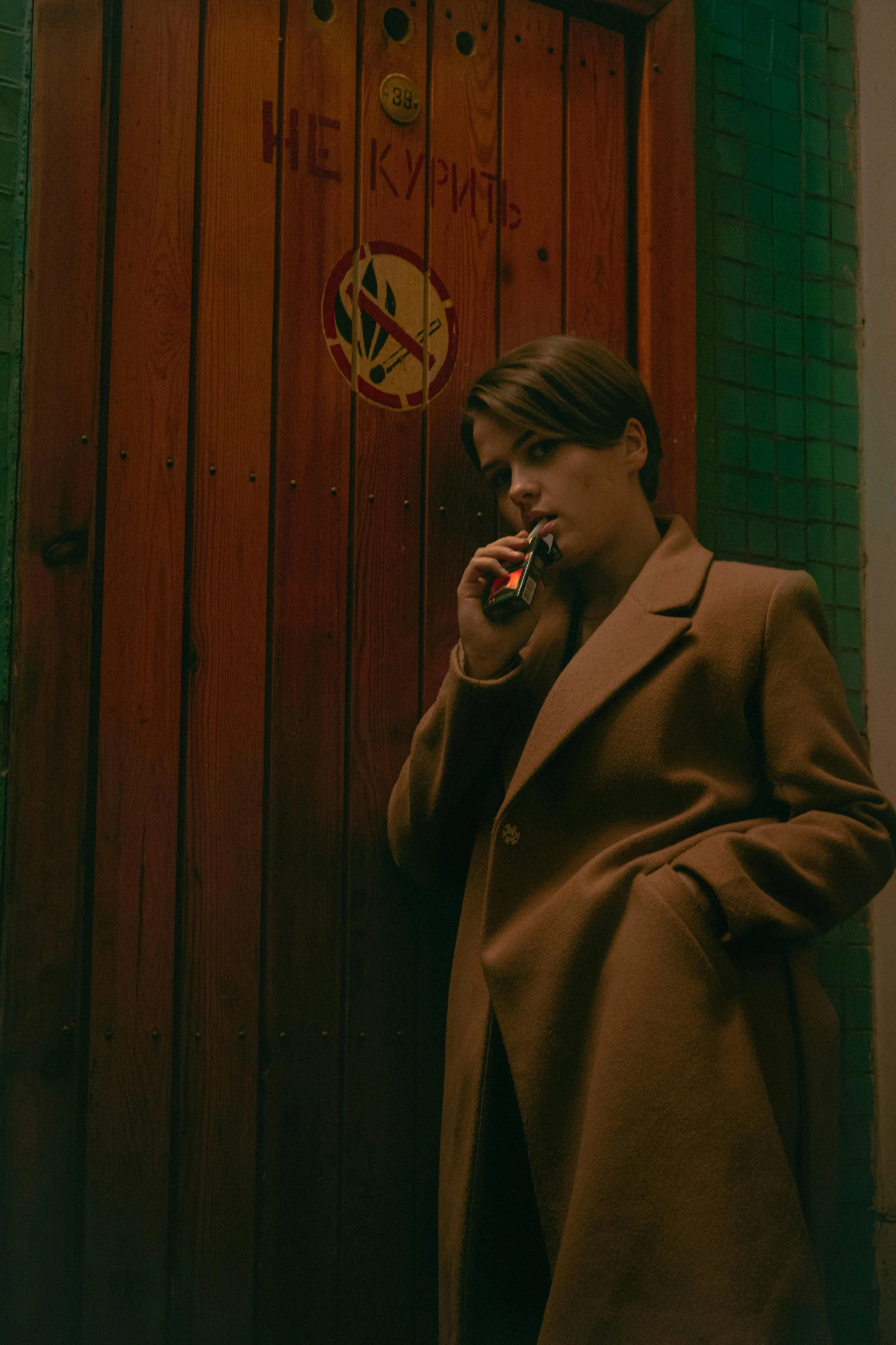 a woman standing in front of a door talking on a cell phone, an album cover, by Elsa Bleda, trending on pexels, bauhaus, mads mikkelsen smoking cigarette, julian ope, jung jaehyun, movie still frame