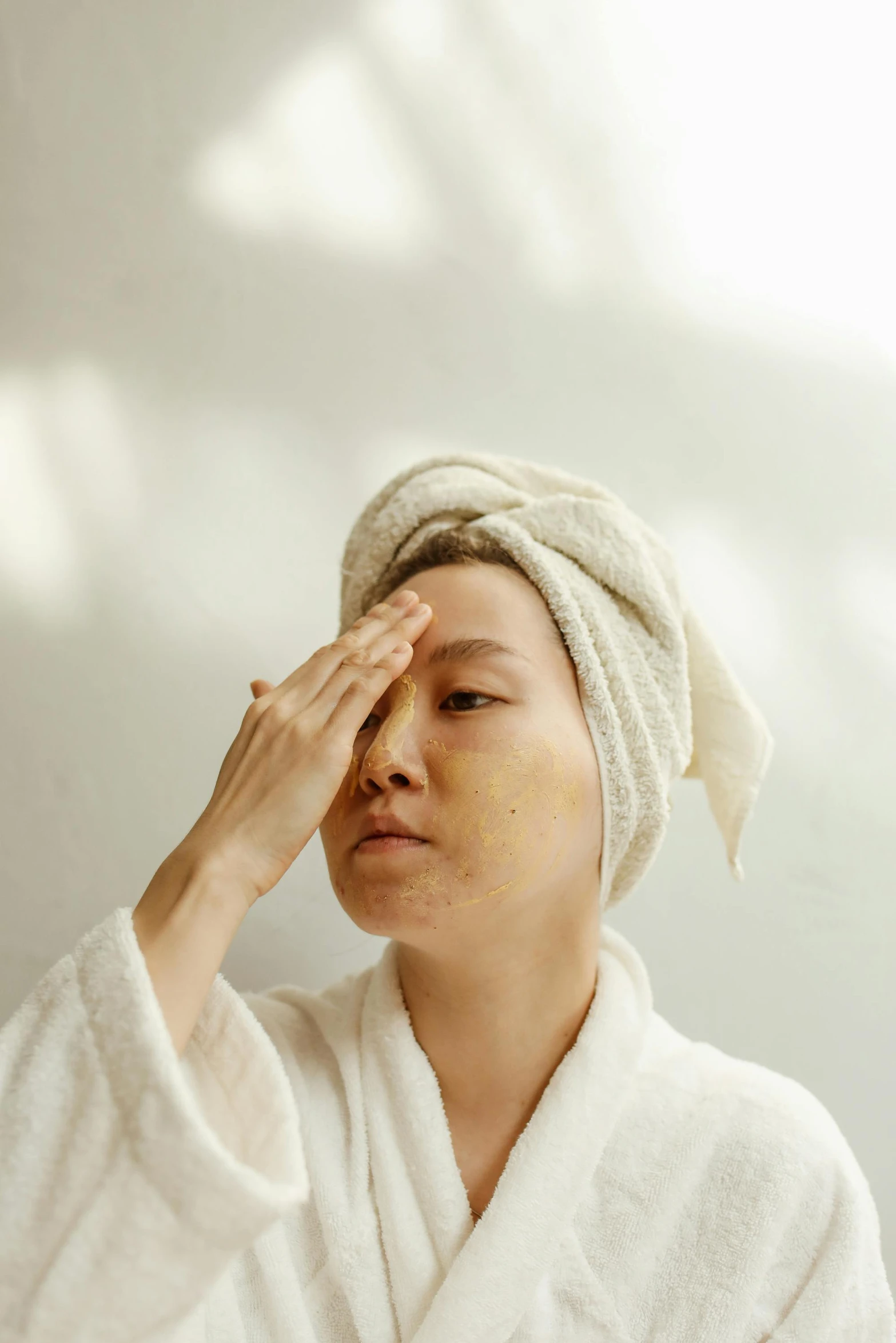 a woman with a towel wrapped around her head, by Matija Jama, trending on pexels, renaissance, asian face, greeting hand on head, surface blemishes, dressed in a robe