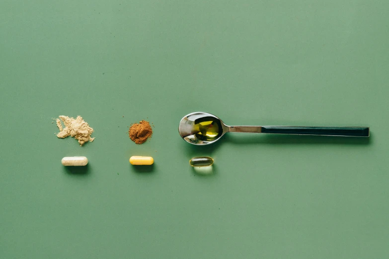 a spoon sitting on top of a table filled with pills, a still life, unsplash, hyperrealism, green and gold palette, ignant, product introduction photo, formulae