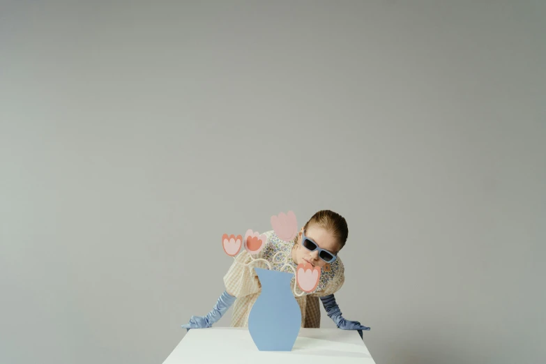 a baby sitting on top of a white table, an album cover, inspired by Méret Oppenheim, trending on pexels, surrealism, charli xcx, hearts, vase with flowers, pose(arms up + happy)