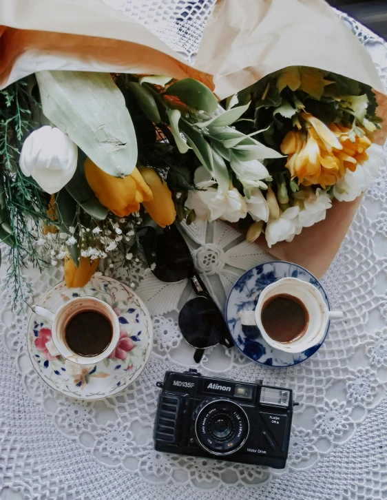 a bouquet of flowers sitting on top of a table next to two cups of coffee, a picture, camera looking down upon, profile image, old picture, uploaded