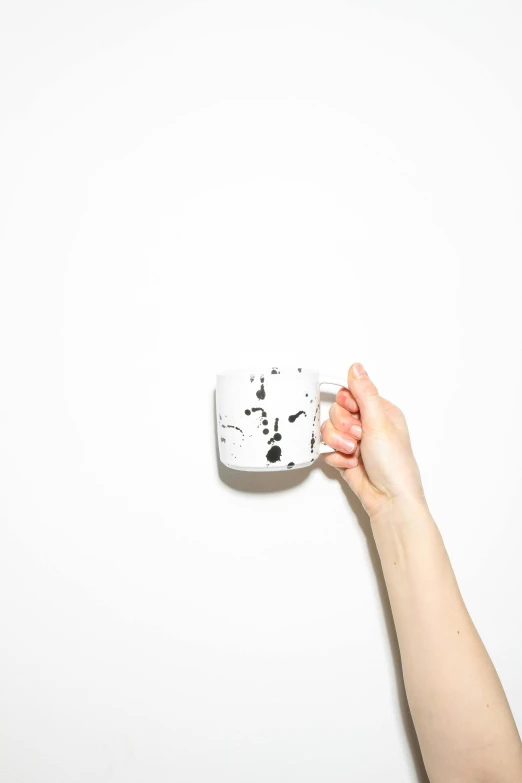 a person holding a coffee cup in front of a white wall, by Lucia Peka, visual art, black splashes, white mug, studio product shot, plan