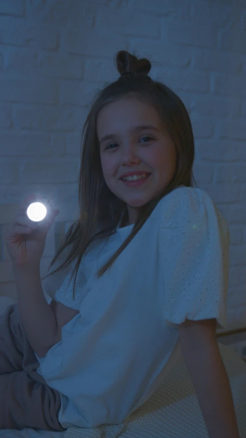 a girl sitting on a bed holding a light, glowing light orbs, tactile buttons and lights, moonlight grey, dark!