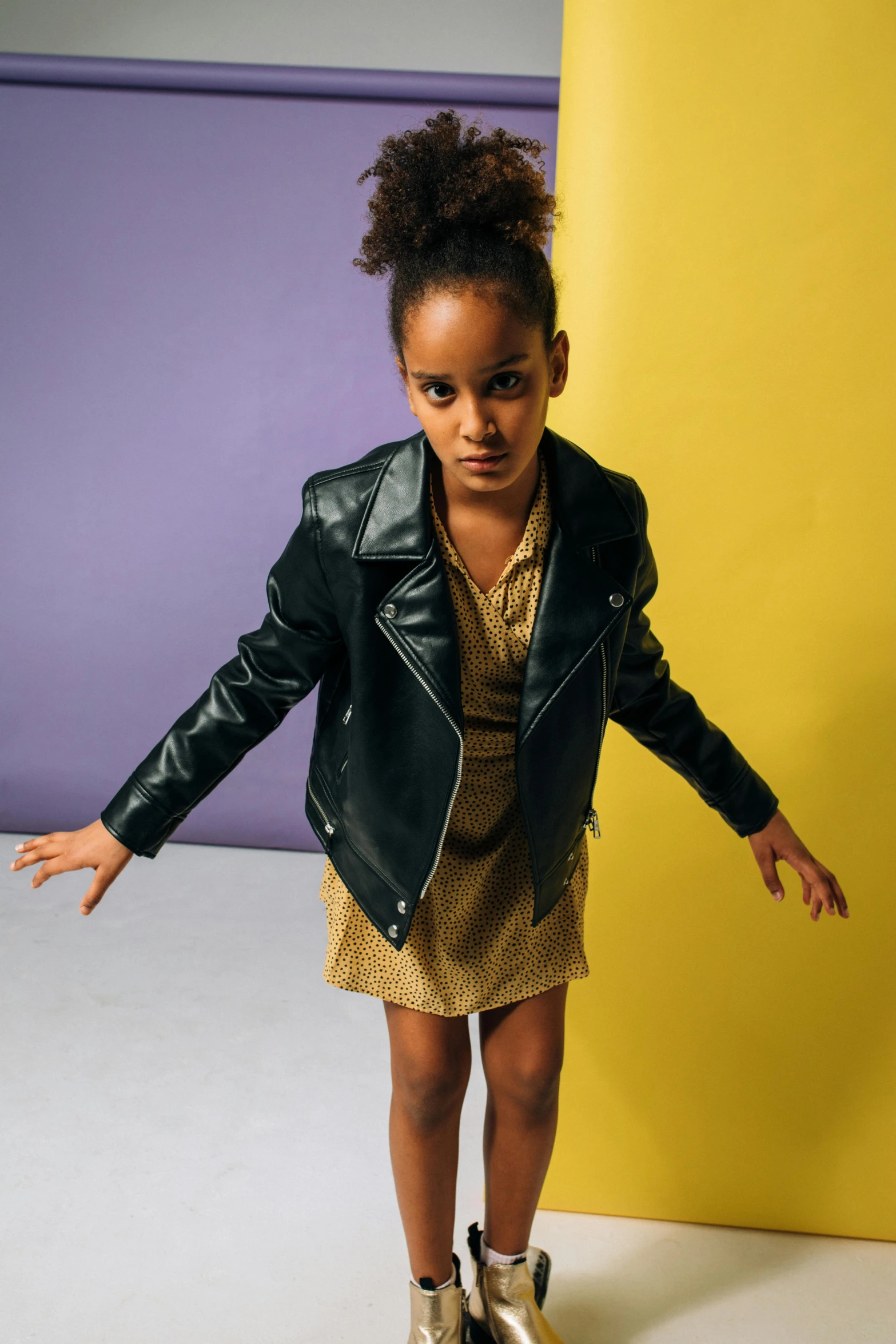 a little girl standing on a skateboard in a room, an album cover, trending on unsplash, dressed in leather jacket, yellow backdrop, an olive skinned, frown fashion model