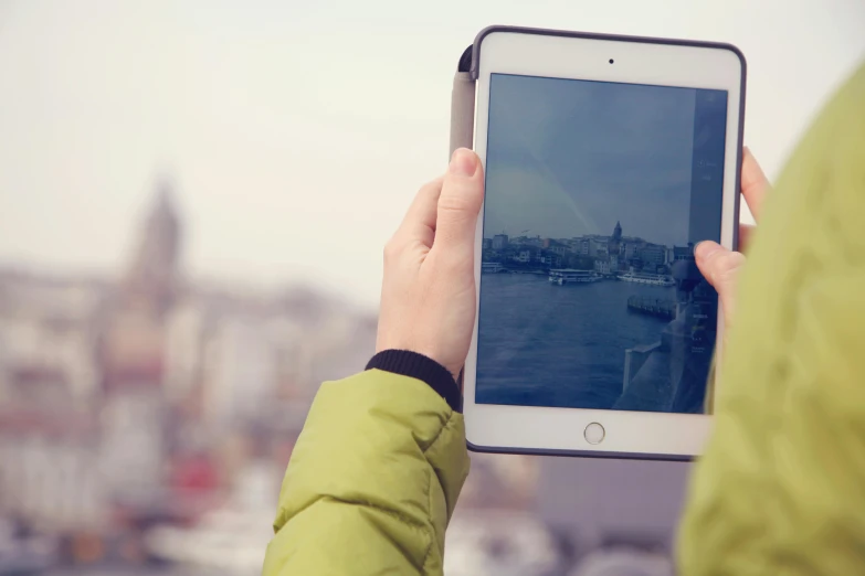 a person holding a tablet with a city in the background, a picture, by Dan Content, trending on unsplash, lomography photo effect, rectangle, tourist, vintage color