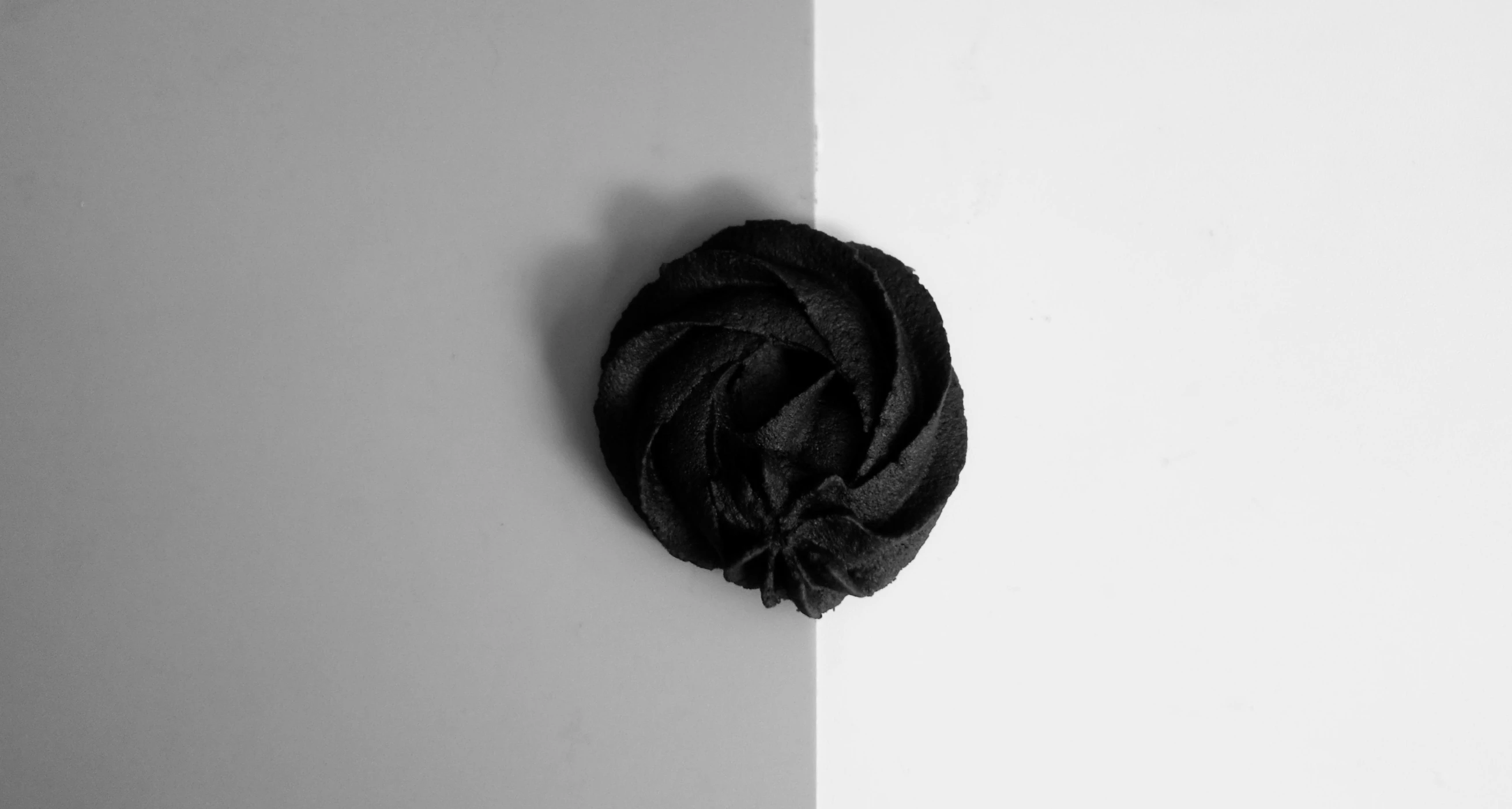 a black rose sitting on top of a white wall, by Emma Andijewska, minimalism, licorice allsort filling, rosette, official product photo, bun )