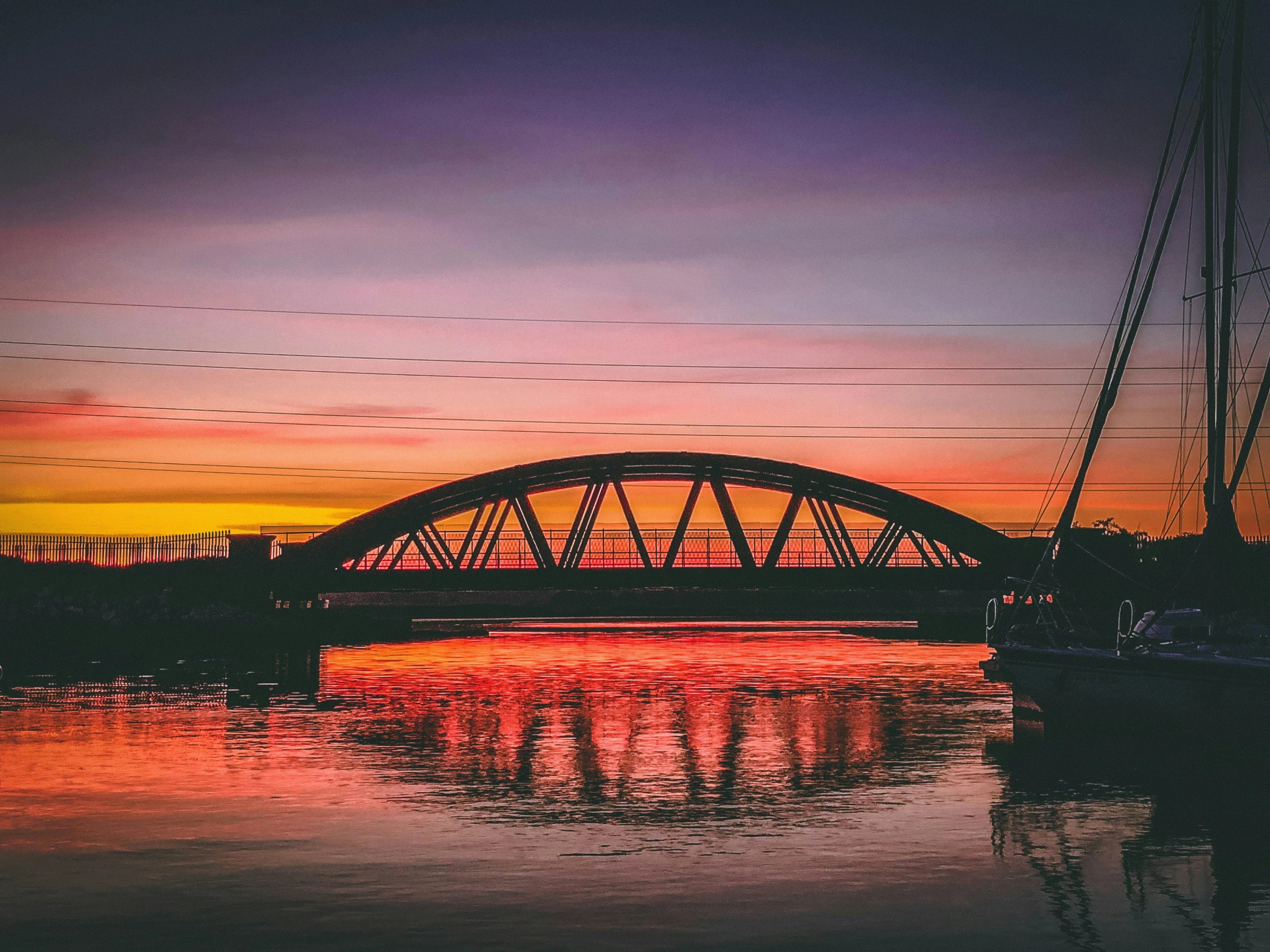 a bridge over a body of water at sunset, by Jan Tengnagel, pexels contest winner, brilliantly coloured, trip to legnica, electricity archs, fully functional