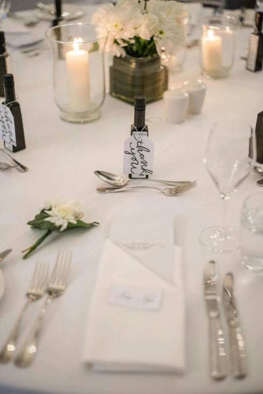 a table that has a bunch of place settings on it, pair of keycards on table, white wine bottle, wedding, up close