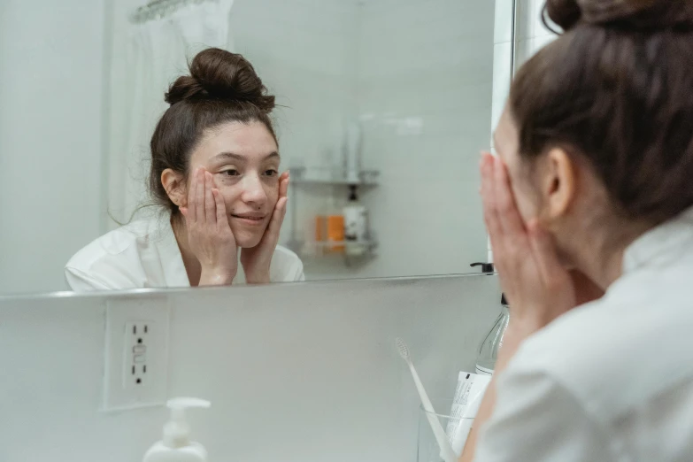 a woman is looking at her face in the mirror, no makeup, embarrassed, photoshoot for skincare brand, doctors mirror