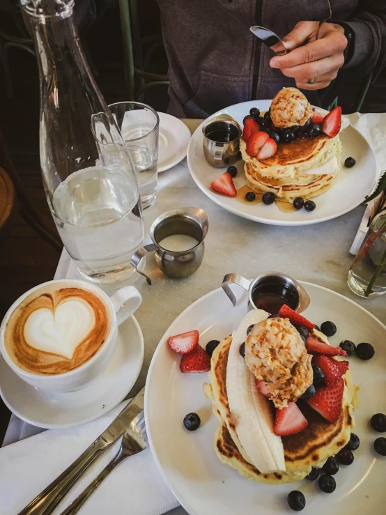 a person sitting at a table with plates of food, pancakes, 🎀 🍓 🧚, aussie baristas, absolutely outstanding image