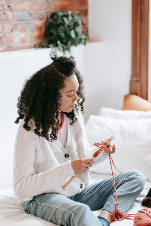 a woman sitting on a bed with a cat, a cross stitch, trending on pexels, mixed-race woman, weaving, wearing a white sweater, curls