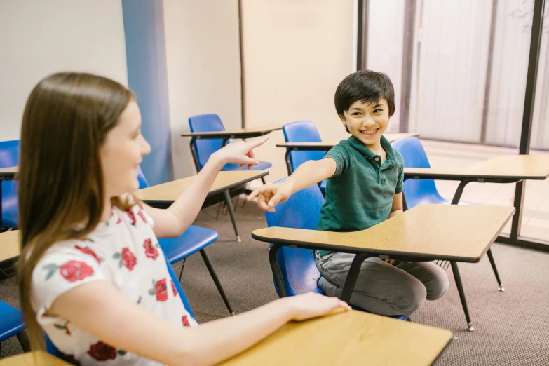 a boy and a girl sitting at desks in a classroom, pexels contest winner, reaching out to each other, lachlan bailey, smiling playfully, product introduction photo