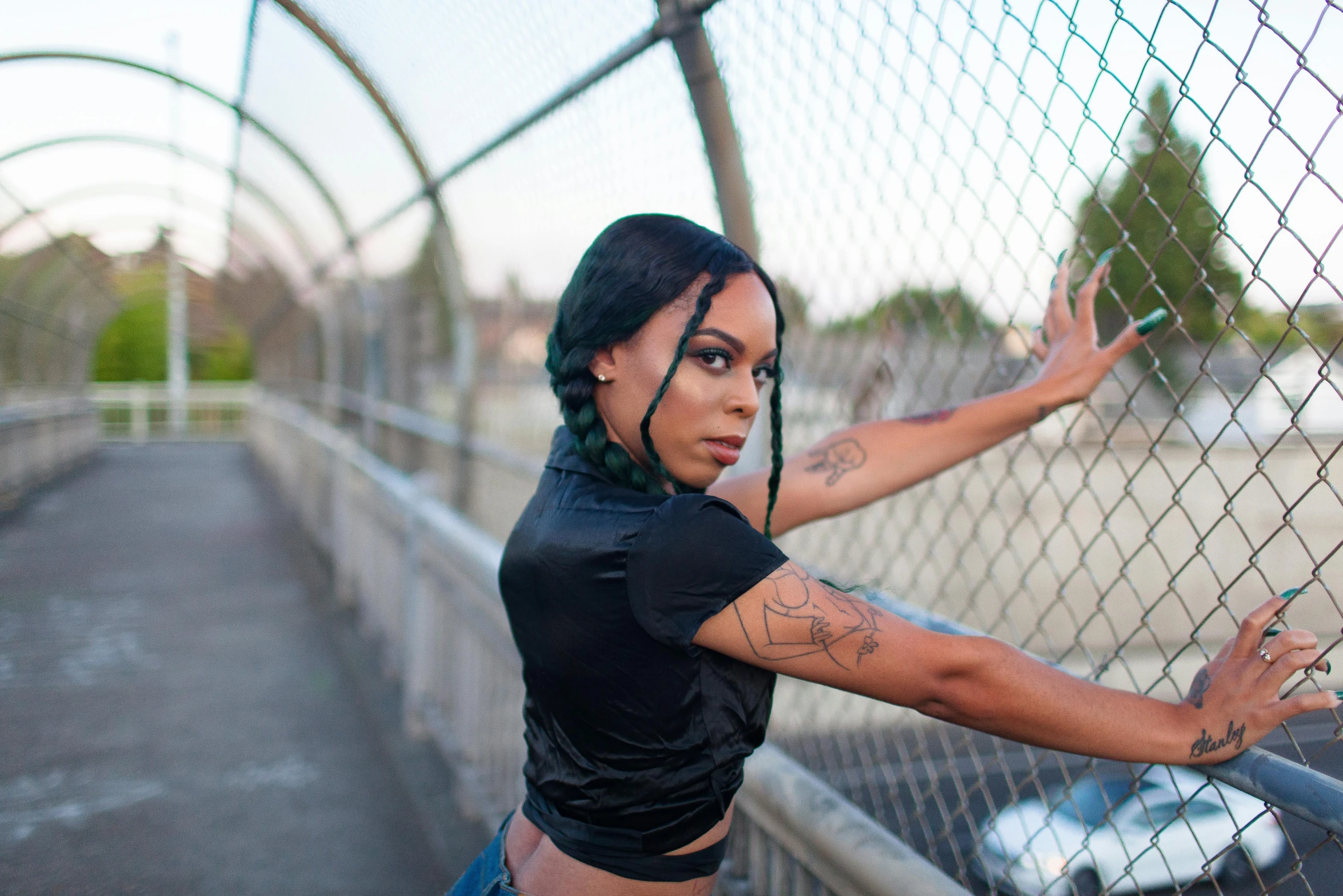 a woman with green hair leaning against a fence, an album cover, unsplash, sexy black woman walks past them, threatening pose, non binary model, bridges