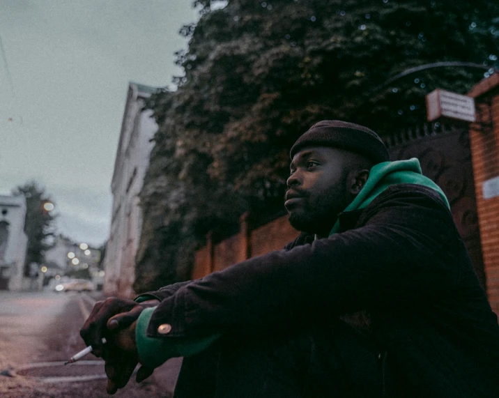 a man sitting on the side of a road, an album cover, pexels contest winner, jaylen brown, looking to the side off camera, mc ride, dark green tones