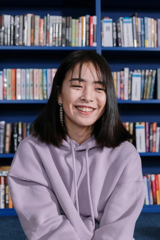 a woman sitting on the floor in front of a bookshelf, inspired by Kim Jeong-hui, pexels contest winner, bjork smiling, pictured from the shoulders up, 1 6 years old, ramil sunga