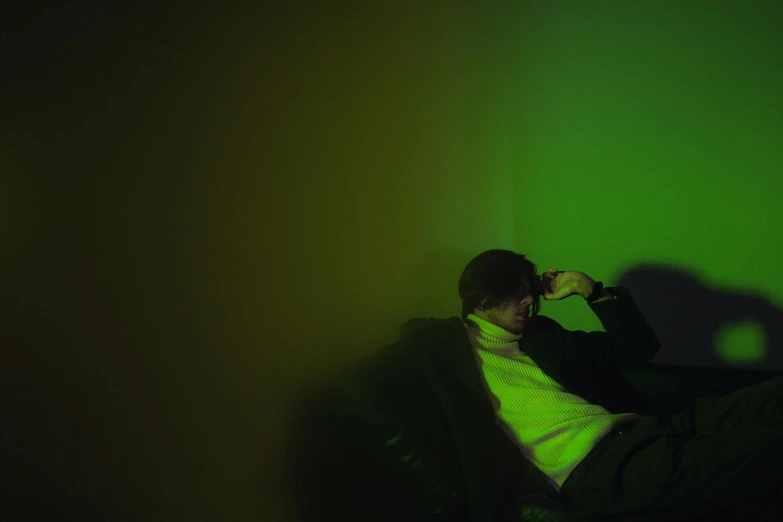 a man sitting in a chair under a green light, declan mckenna, colour photograph, relaxing on the couch, color photograph