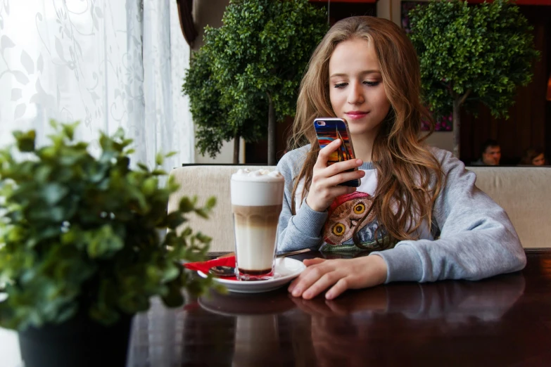 a woman sitting at a table looking at her cell phone, a portrait, by Julia Pishtar, trending on pexels, happening, teenager girl, sitting on a mocha-colored table, 15081959 21121991 01012000 4k, cutest