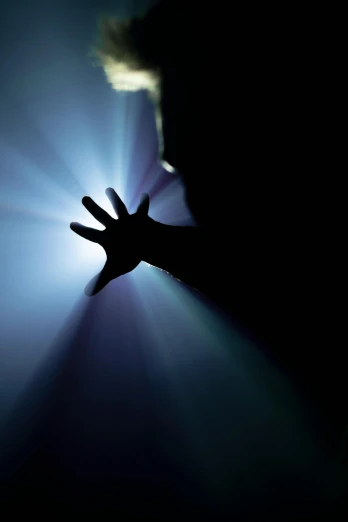 a person holding their hand up in the dark, light and space, harsh overhead sunlight, silhouetted, dim blue light, flashlight on