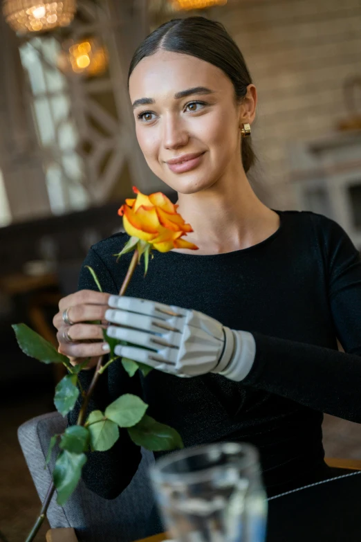 a woman sitting at a table with a rose in her hand, wearing bionic implants, leather gloves, linen, grey