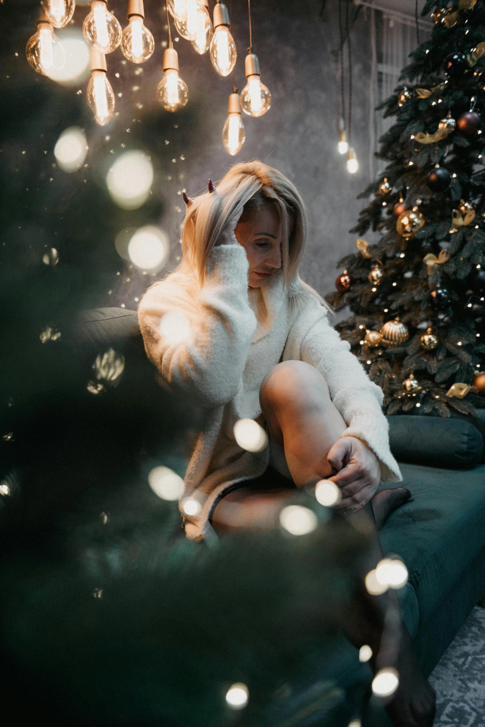 a woman sitting in front of a christmas tree, pexels contest winner, wearing a white sweater, flickering lights, blonde women, gif