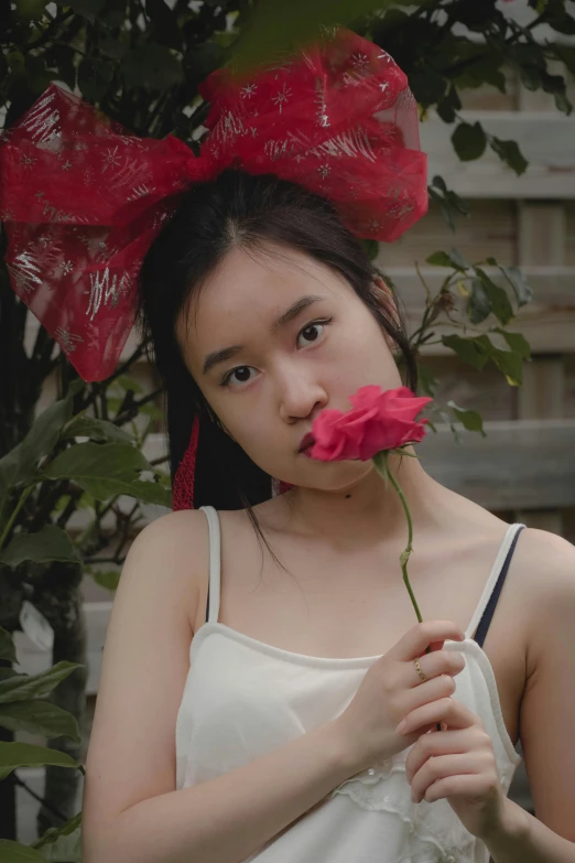 a woman holding a flower in front of her face, an album cover, inspired by Feng Zhu, unsplash, a red bow in her hair, still frame from a movie, she is about 1 6 years old, low quality video