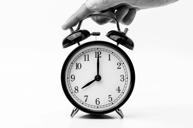a black and white photo of a hand holding an alarm clock, set against a white background, background image, uploaded, countdown