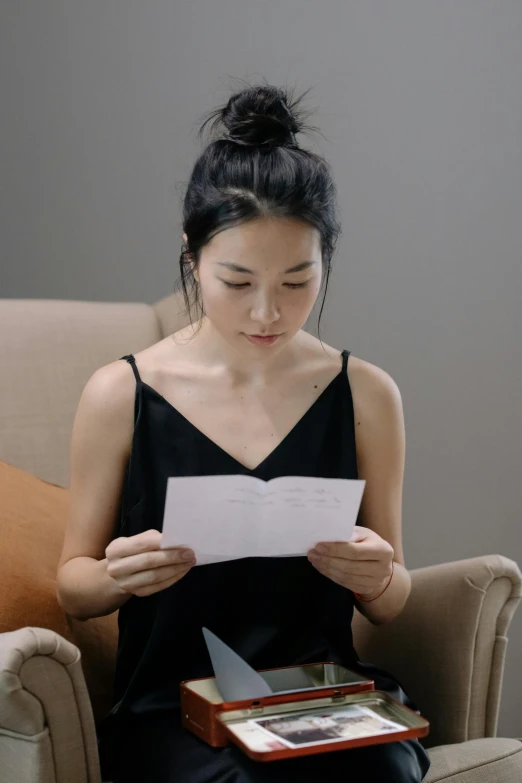 a woman sitting in a chair reading a piece of paper, by helen huang, pexels contest winner, letterism, wearing a cropped black tank top, asian face, video, elegant study