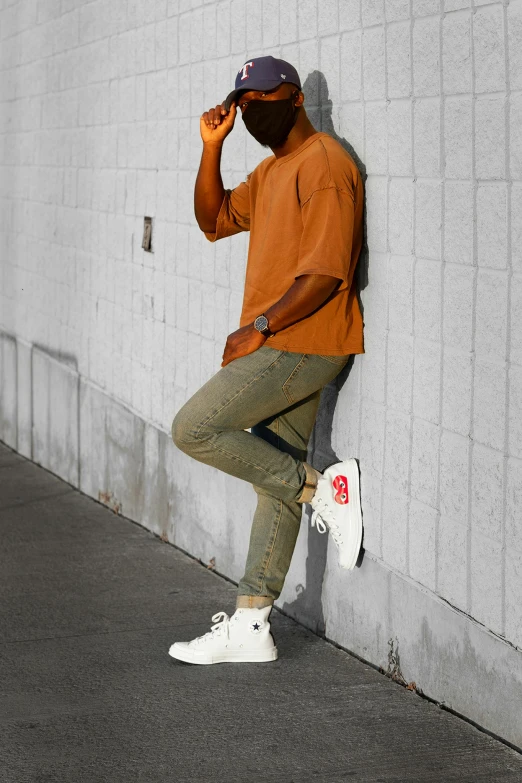 a man leaning against a wall with a skateboard, inspired by Theo Constanté, trending on pexels, happening, green and brown clothes, orange hue, view(full body + zoomed out), promotional image