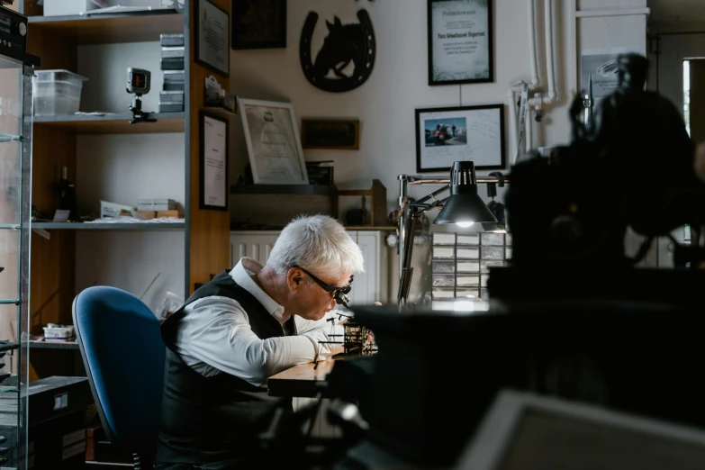 a man sitting at a desk working on a computer, a photo, pexels contest winner, private press, silver jewellery, gunsmithing, local conspirologist, profile image