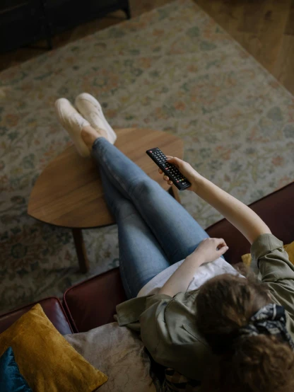 a woman sitting on a couch holding a remote control, by Carey Morris, trending on pexels, happening, wearing jeans, on a table, 15081959 21121991 01012000 4k, girls resting