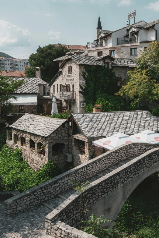 a stone bridge over a river with buildings in the background, inspired by Sava Šumanović, sharp roofs, a high angle shot, shed roof, bosnian